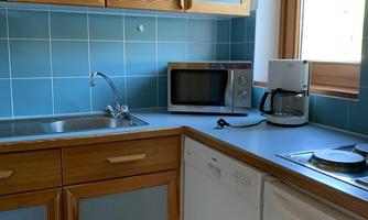 A modern kitchen with wooden cabinets and blue tiles. On the countertop, there is a microwave, a coffee machine, and a cooktop.