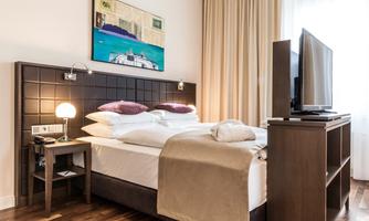 A modern hotel room with a large bed, a TV, and a nightstand. Warm colors and a painting give the room an inviting atmosphere.