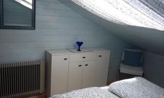 A cozy bedroom with wooden paneling and a warm color scheme. There is a bed with floral bedding, a wardrobe, and a chair.