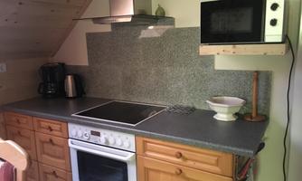 A modern kitchen with wooden cabinets and a gray countertop. Visible are a stove, a microwave, and a coffee maker.