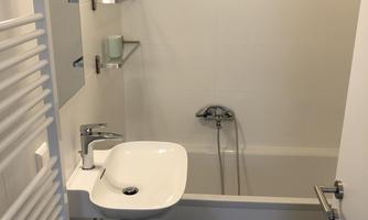 A small bathroom with a bathtub and a sink. There is also a towel heater on the wall.