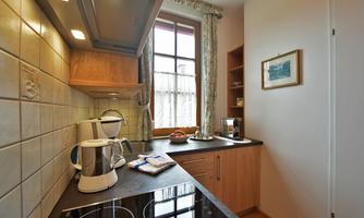 A modern kitchen with light wood cabinets and a wooden countertop. A kettle and a coffee machine are on the counter, and light streams in through a large window.