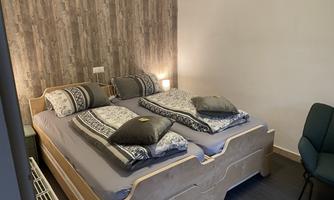 A cozy bedroom with a double bed and pillows. The walls are designed with a wood look and there is a chair in the corner.