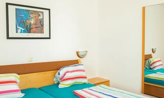 An inviting bedroom with a double bed and colorful pillows. A modern artwork hangs on the wall, and a mirror reflects the cozy atmosphere.