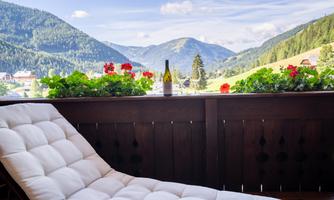 A cozy balcony with a lounger and blooming flowers. In the background, the majestic mountains can be seen.