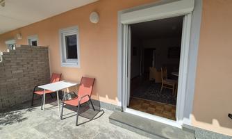 A terrace with two red chairs and a table. In the background, an open room can be seen.