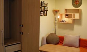 A cozy living space with a red sofa, a table, and an open closet. The walls are designed in soft colors with decorative elements.