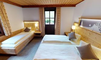 A bright room with two beds and a cozy seating area. The walls are made of wood and large windows provide plenty of daylight.