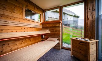 A cozy wooden sauna with a large window overlooking the green meadow. The benches are simply designed and invite relaxation.