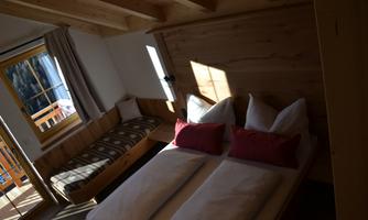 A cozy bedroom with two beds and a daybed. The wood paneling and natural light create a warm atmosphere.