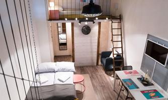 A modern, minimalist apartment with a cozy bedroom upstairs. The living area has a comfortable sofa and a dining table.