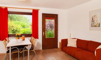 A cozy living space with a table, chairs, and a red sofa. Large windows let in plenty of light and a view of the garden.