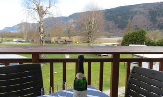 A beautiful view from a balcony overlooking a green meadow and mountains in the background. On the table, a bottle of champagne and two glasses are ready.