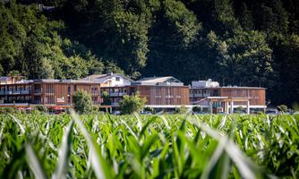 A modern building amidst tall fields. In the background, trees and hills can be seen.