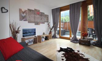 A cozy living room with a gray sofa and red cushions. Large windows allow plenty of light in and provide a view of a small balcony.