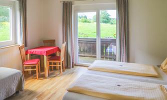 A bright room with two beds, a table, and chairs. Large windows offer a view of the green landscape.