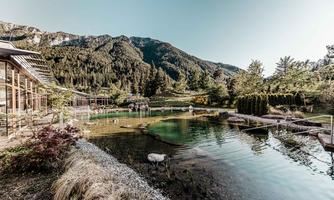 A quiet pond surrounded by green mountains and trees. In the background, modern buildings are visible, creating a relaxing atmosphere.