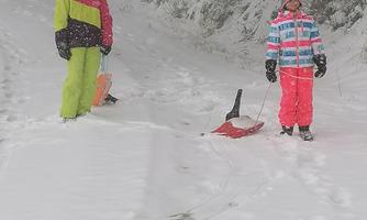 Two children are standing in the snow wearing colorful winter clothing. They are ready to go sledding in a snowy landscape.