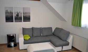 An inviting living room with a grey couch and a modern coffee table. Three pictures hang on the wall, and the room has green curtains.