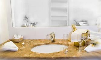 An elegant bathroom with a marble washstand. On the surface, there are glasses and a bottle of champagne, surrounded by white towels.