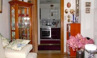 A cozy living area with a bright sofa and a display cabinet. In the background, a modern kitchen with a stove and decorative elements can be seen.