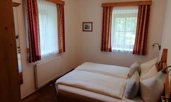 A cozy bedroom with two single beds and bright curtains. The room has a warm wooden design and plenty of daylight.