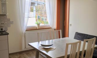 A bright dining room with a table and chairs. The window provides plenty of daylight and the kitchen is nearby.