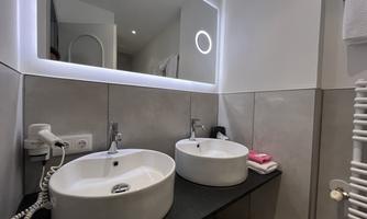 A modern bathroom with two round sinks on a dark countertop. The illuminated mirror creates a pleasant atmosphere.