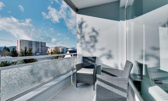 A balcony with two modern chairs and a beautiful view. The sky is blue with some clouds.