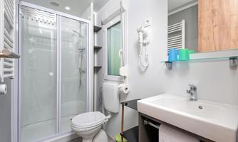A modern bathroom with a shower, a sink, and a toilet. The walls are bright and there are practical storage spaces.