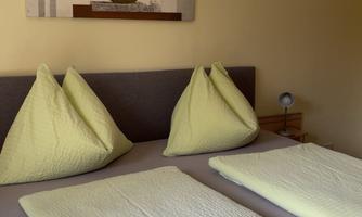 A cozy bedroom with two beds and green pillows. A decorative picture hangs on the wall.