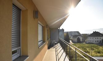 A balcony with a view of the surroundings. The morning sun is shining and there is a green meadow in the background.