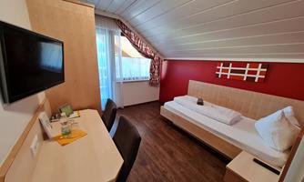 A cozy room with a single bed and a desk. A large window front provides plenty of daylight and a nice view outside.