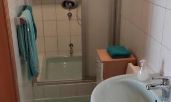 A small bathroom with a shower and a sink. The tiles are light green, and there are some towels in different colors.