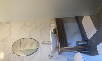A modern bathroom with a stylish wooden sink shelf. The walls are tiled with light tiles and a large mirror is present.