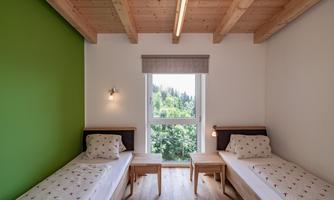 A cozy room with two single beds and a large window. The walls are painted in calming colors, with a green accent wall.