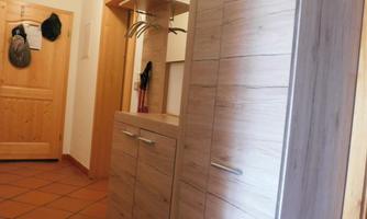 A narrow hallway with a modern wooden cabinet and a light wall. In the background, a wooden door is visible.