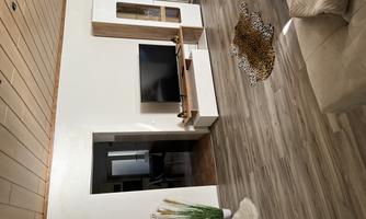 A modern living room with a television on a white TV cabinet. The room has a light wood floor and a cozy atmosphere.