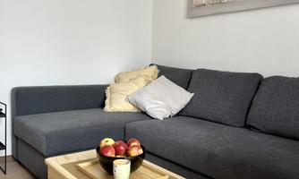 A cozy living room with a gray sofa and a wooden table.  
On the table, there is a bowl of apples and a vase.
