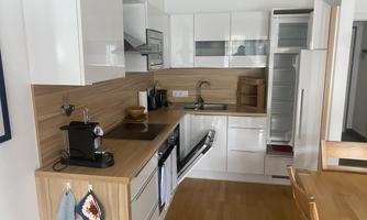 A modern kitchen with white cabinets and wooden accents. There is a cooking area, a refrigerator, and a dining area.