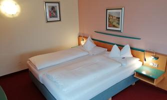 A cozy bedroom with two single beds and decorative pillows. The walls are painted in soft colors and there are artworks on the walls.
