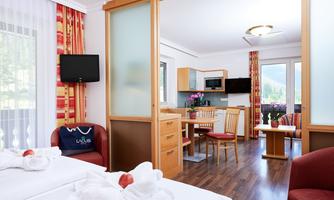 A cozy room with two beds and modern furniture. The kitchen and living area are open and bright with large windows.