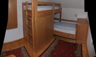 A cozy bedroom with a wooden loft bed and a single bed. The room has a carpet and a warm atmosphere.