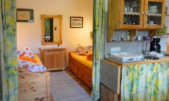 A cozy room with wooden furniture and two beds. The kitchen is modern and well-equipped, surrounded by colorful curtains.
