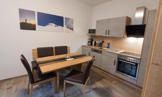 A modern kitchen with a dining table and chairs. Three pictures hang on the wall and the kitchen is well-equipped.