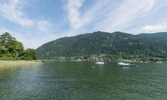 A tranquil lake overlooking green hills. In the water, there are some boats, and the sky is blue with a few clouds.