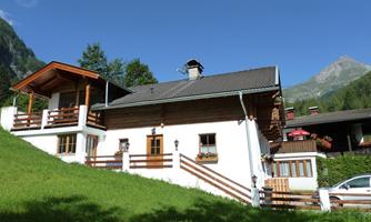 A lovely chalet in the mountains with a large garden and terraces. In the background, green slopes and a mountain can be seen.