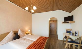 A cozy bedroom with two beds and a warm wooden ceiling. A TV hangs on the wall and a small table stands next to a chair.