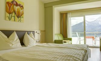 A bright hotel room with two beds and a picturesque view of the mountains. The room is decorated with a modern seating area and a floral picture.
