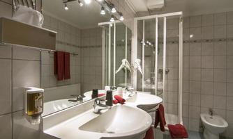 A modern bathroom with two sinks, a shower, and a toilet. The walls are tiled, and colorful towels give the room a fresh accent.
